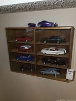 Front view of wooden display case mounted on wall showing eight diecast model cars inside and glass sliding doors.