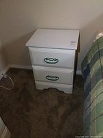 White nightstand with green handles beside a bed, showing overall design and size.