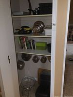 Overview of kitchen closet contents showing pots, pans, cookbooks, and kitchen accessories on shelves and hanging hooks.