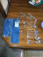 Overview of flatware assortment: spoons, forks, napkin ring, pouches on wooden table