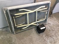 Underside view of small folding table showing metal legs folded up and table frame, heater placed beside it on the floor.