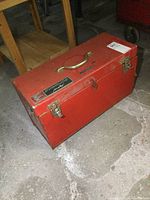 Closed red metal toolbox with two silver latches, brass handle, Evinrude branding on top