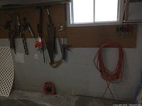 Wide view showing electric hedge trimmer, hand saws, hammer, and other tools hanging on pegboard, also orange extension cords coiled and hanging