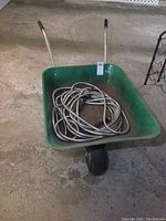 Green metal wheelbarrow with black tire and handles seen from front, hose inside