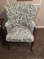 Front view of wing back chair showing floral upholstery and wooden legs.