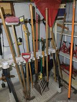 Full view of the Suncast yard tool rack with various garden tools held in place including hoes, shovels, fork, rakes, broom, and pole limber.