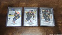Front view of three Connor McDavid rookie cards in protective plastic cases, showing player in action.