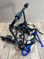 Black metal and plastic CCM tri bike rack with foam padding and straps, arranged on wooden surface with neutral background, shows wear and components.