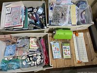 Three plastic bins filled with assorted stamps, paints, adhesives, stencil sheets, embellishments and craft papers. Manual paper cutter and green plastic tool placed beside bins.