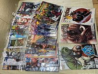 View of assorted comic books in clear plastic covers laid out on a table, showing various character covers including Venom and Avengers.