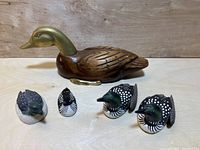 Photo showing one large wooden and brass duck and four smaller painted ducks in various patterns on a wooden surface