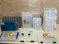 Wide shot showing 14 fishing tackle boxes in various sizes and brands on wooden surface.