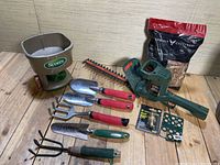 Photo showing all items together including hedge trimmer, seed spreader, hand tools, wood chips, propane torch ignitor, and plant markers.