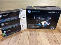 HP Photosmart printer box and four HP LaserJet 131A toner cartridge boxes on wooden floor.