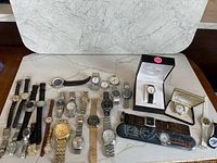 Overhead image showing 25 assorted wristwatches on white surface including boxed watches and loose watches with various straps