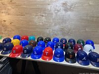 Front row of miniature baseball helmets arranged in a row showing team logos such as Dodgers, Tigers, Rangers, Royals, Yankees, Giants