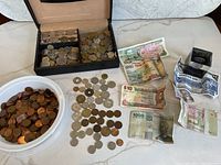 Wide view showing all coins, banknotes, black display box with coins, and white container filled with copper coins