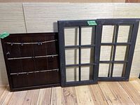 Two wooden picture boards and two black wooden window frame panels displayed on wooden floor and leaning against wall