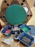 Poker table with chips and cards arranged in front of table. Table is octagonal wood with green felt center showing wear. Four plastic bins hold chips in red, green, black, and white. A rotating chip tray with chips and a gray card case with multiple decks are included.