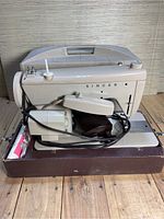 Singer sewing machine with case and attached cord inside brown base