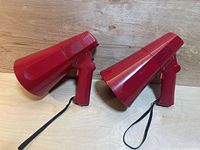 Two red transistor megaphones side by side on a wooden surface.