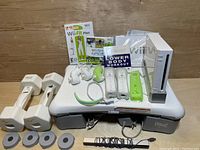Wii console, Wii Balance Board, 2 Everlast dumbbells, 2 Wii Remotes with wrist straps, 2 Nunchuks, Wii Fit Plus and Wii Sports game cases, Lower Body Workout booklet, 4 Wii Balance Board weights, and sensor bar all arranged together.