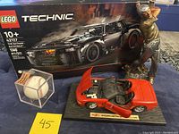 Photo of LEGO Technic The Batman Batmobile in box, autographed baseball in display case, red Maisto Corvette diecast model with open hood, and golfer statue missing club.
