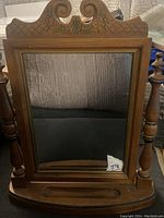 Full view of vintage wooden standing tilt vanity dressing mirror with decorative carved top and turned side supports.