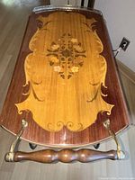 Close-up of rectangular top with central floral golden inlay and wooden handle with brass details