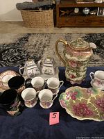 Full view of assorted fine china pieces including cups, teapot, cream and sugar set, and plates placed on a table.