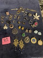 Photo showing assorted rings, brooches, pendants and earrings on a dark cloth background with a pink lot number.