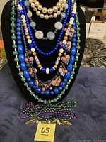Multiple vintage and handmade beaded necklaces displayed on a black bust and colorful metallic bracelets laid flat on surface