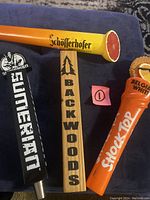 Four beer tap handles displayed on blue surface featuring Shock Top, Schofferhofer, Backwoods, and Sumerian Brewing Co brands.