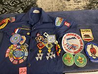 Front of blue Boy Scouts of America uniform shirt showing various patches including Great Activities Patch, Order of the Arrow, troop and committee insignia, and decorative pins and beads.