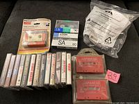 Photo showing cassette player cleaner in package, two unopened blank cassette tapes, several music and children's cassette tapes, and packaged children's USB headphones.