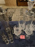Clear glass decanter with stopper, four cut lead crystal wine glasses, five gold rim shot glasses on table