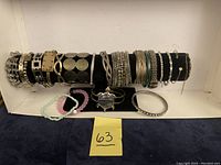 Full view of all bracelets arranged on black bracelet display with few additional stretch and charm bracelets in front on white surface.