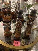 Three hand carved folk art figures on glass table - two Korean village guardians with painted faces and carved Korean script, and one totem pole with carved and painted face and bird on top.