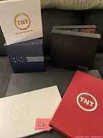 Photo of the seven DVD box sets including 2 from HBO, 3 from TNT, and 1 from Warner Bros Television Studios on a couch.