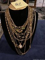 Photo showing multiple layered gold tone necklaces on a black necklace display stand, highlighting a variety of chain styles and pendants.