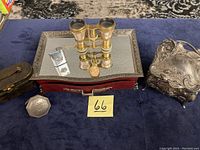 Photo of antique vanity items on dark blue fabric including jewelry boxes, opera glasses, and silver-tone ornate box