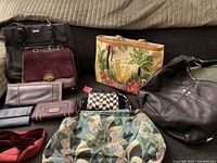 Seven handbags and wallets arranged on a sofa showing colors, styles, and conditions