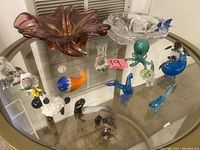 Wide view of vintage lead crystal dish, mauve blown glass dish, and multiple miniature animal and sea life glass figurines on glass table