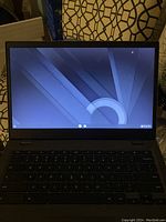 Front view of Lenovo Chromebook powered on showing lock screen or screensaver with geometric wallpaper.