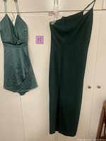 Two women's dresses hanging, one dark green silky short dress and one black one-shoulder long dress