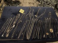 Full view of 18 silver tone necklaces displayed on dark surface showing different chain lengths, styles, and pendants