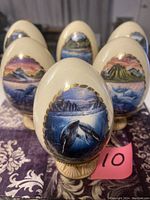 Photo showing the front of six porcelain eggs hand painted with marine life and coastal scenes, each on a stand, arranged in a triangle formation.