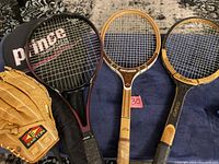 Photo showing all items: Prince Graphite Lite XB Oversized tennis racket with black cover, Centurion Special Selected Frame wooden racket, Wilson Advantage racket, and Easton baseball glove.
