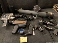 Full lot view showing two vintage handheld movie cameras (Sears 8mm silver camera and Bell & Howell black and gold camera), multiple camera lenses including a long Soligar lens, various lens caps and mounts, and parts of a Galileo telescope including black cylindrical components.