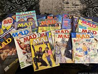 Over 30 vintage MAD magazines displayed fanned out on a patterned carpet, showing colorful illustrated covers with various themes from early to mid 1990s.